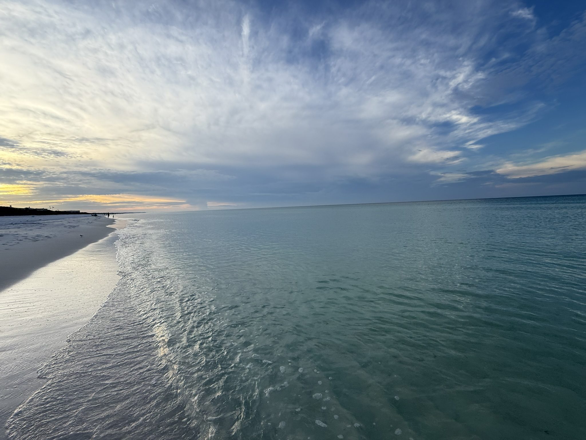 Glassy, gin-clear Gulf water at dusk along an almost empty white sand beach
