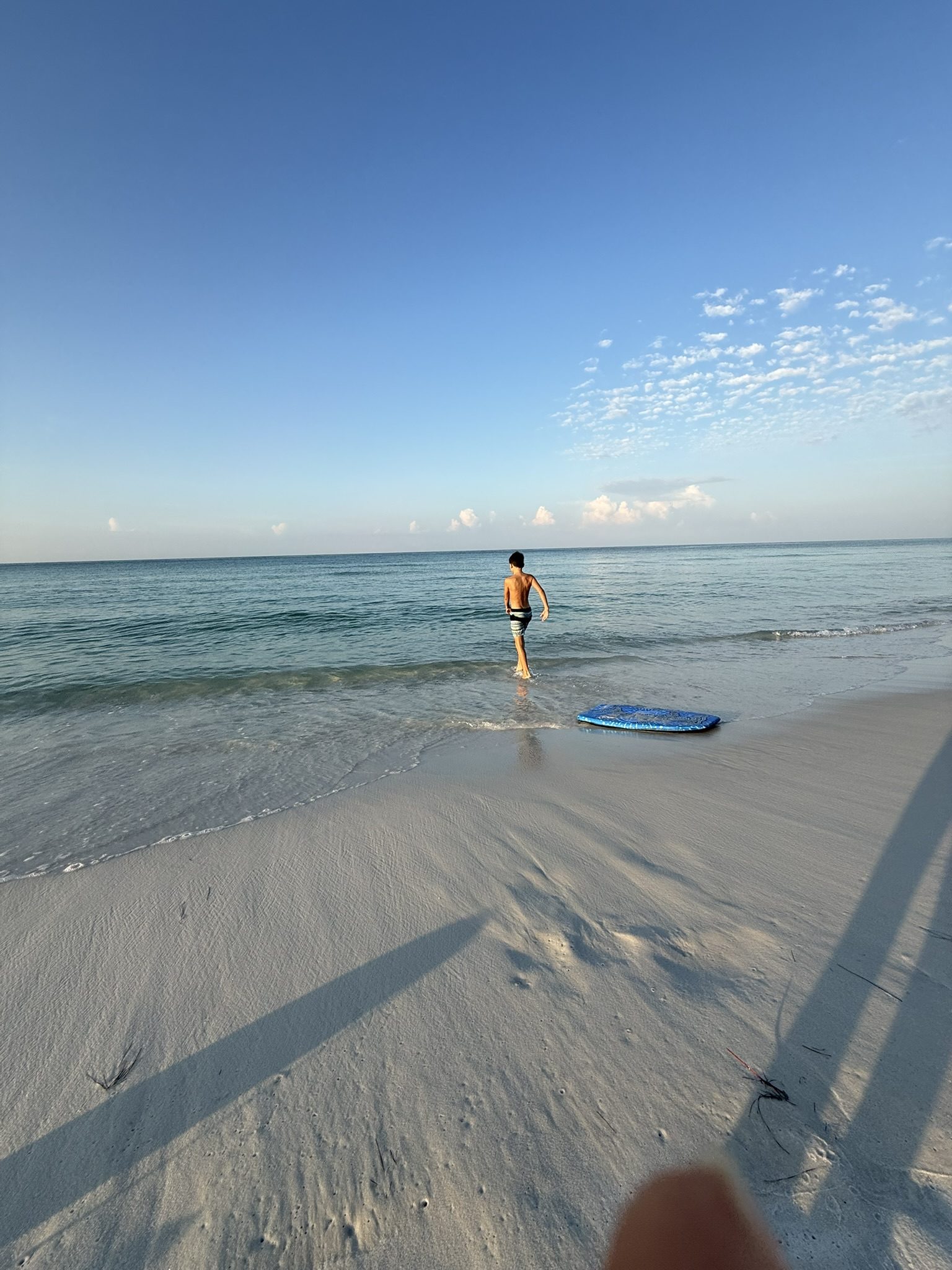 A boy running into calm morning surf on an empty white sand beach, boogie board waiting at the waterline