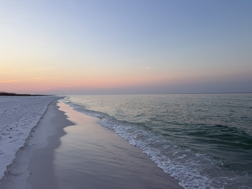Empty white sand beach under a pastel pink and lavender sky, not a person or building in sight