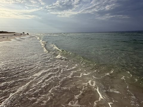 Gentle surf washing over white sand with two distant figures far down the empty beach
