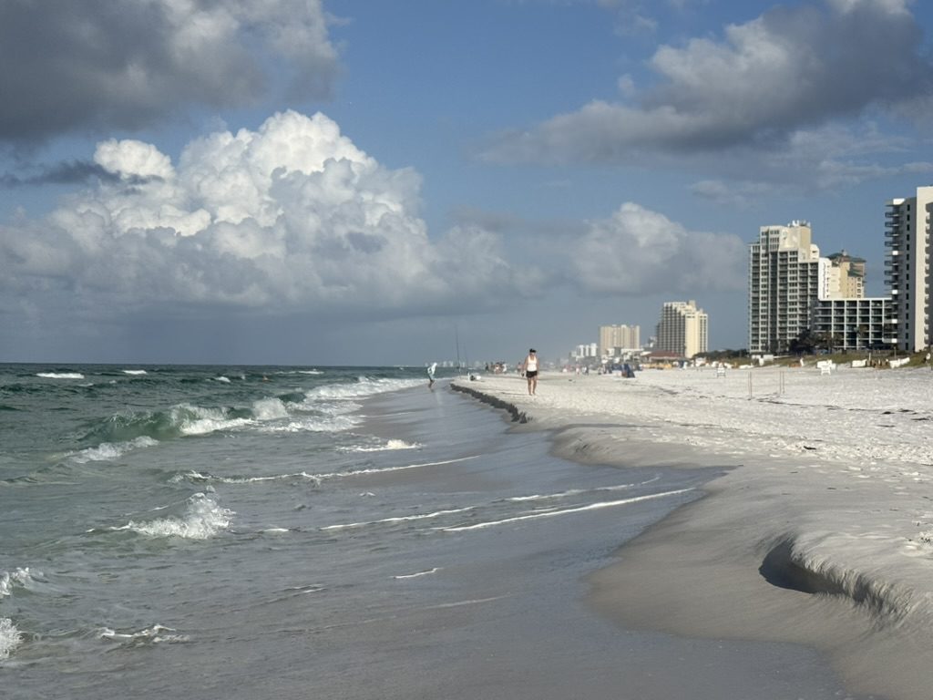 Wide, nearly empty white sand beach in the foreground with the high-rise skyline beginning far down the shore
